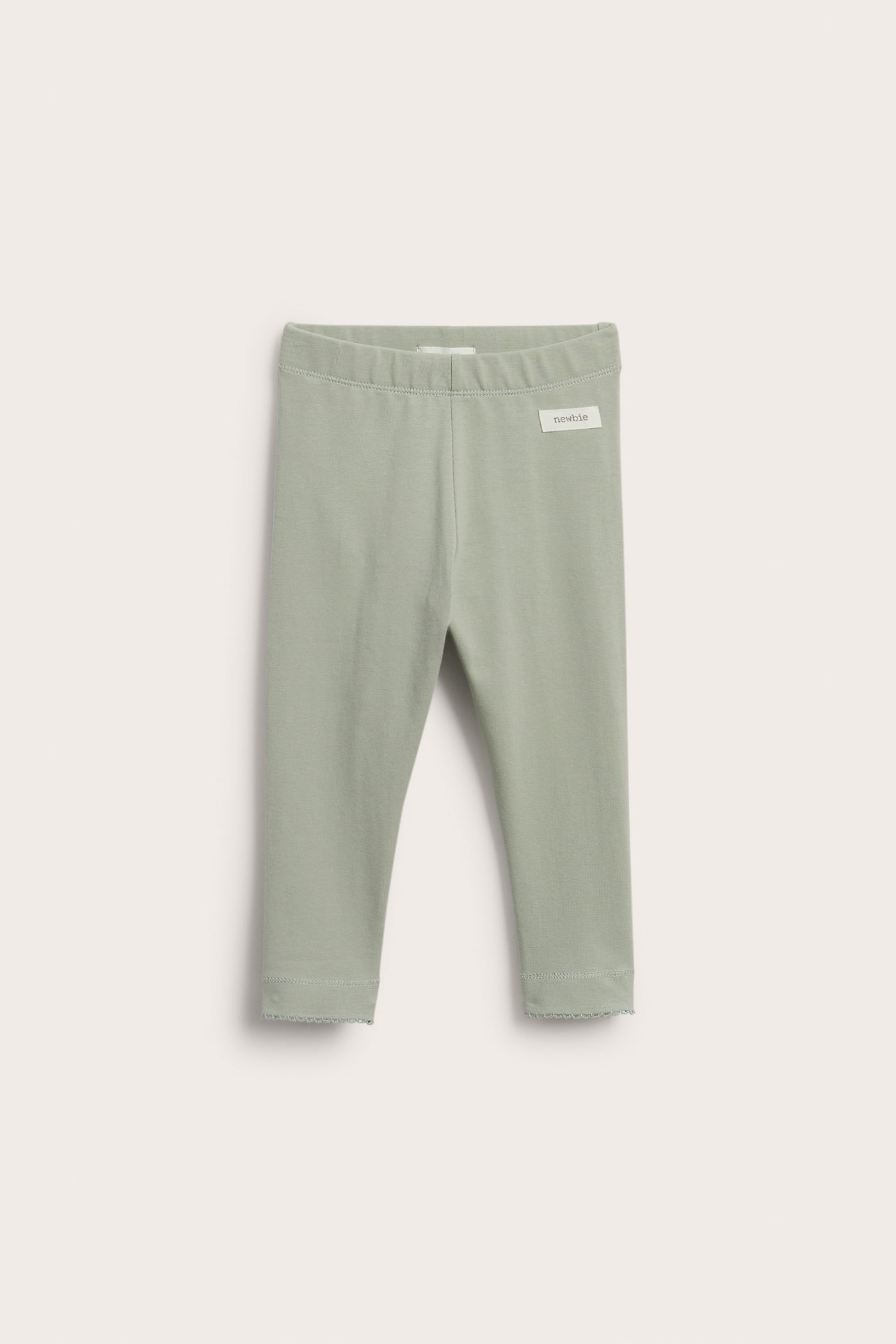Front view of baby's light green leggings with an elastic waist and scalloped ankle edges.
