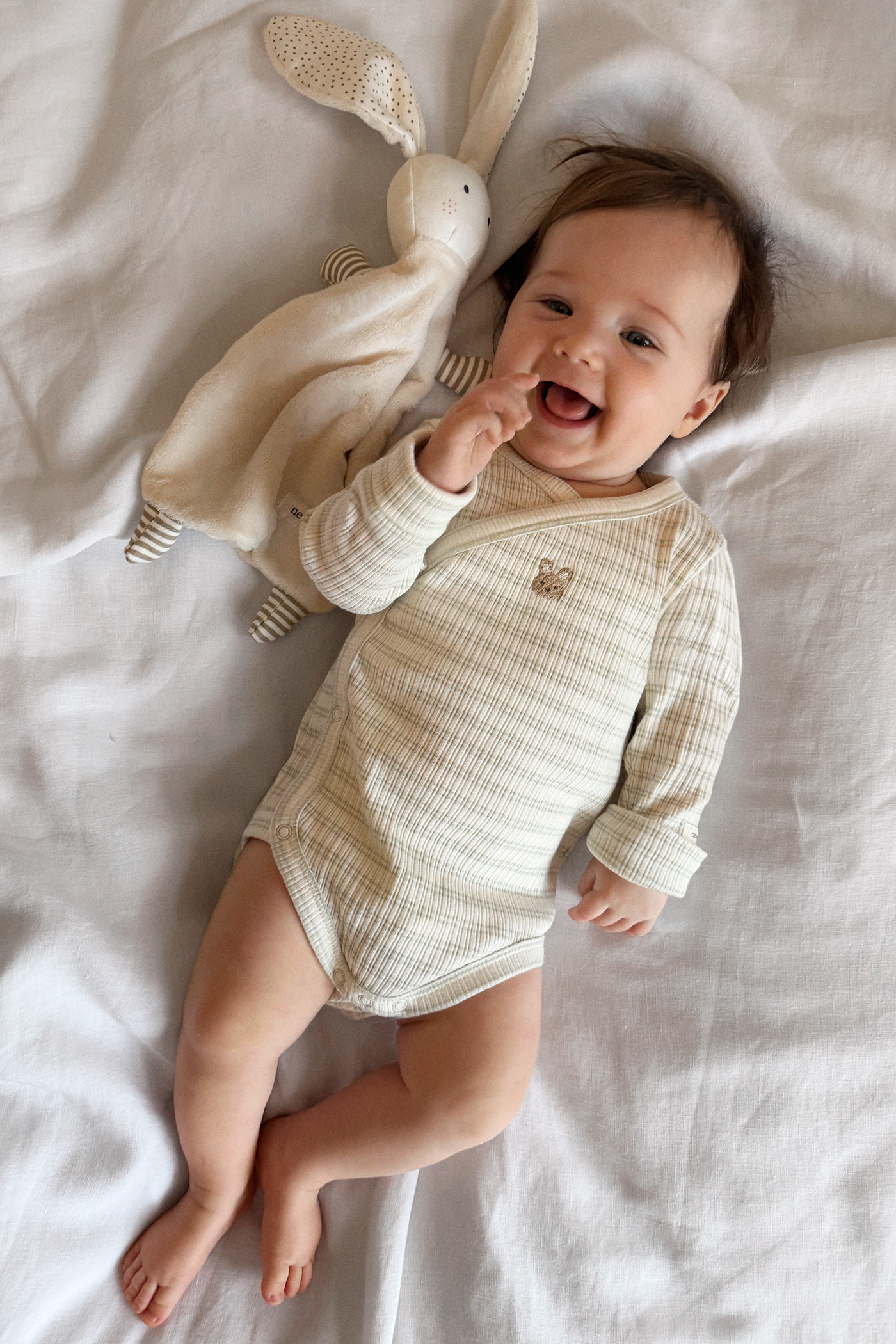 Babyjunge, der mit einem Schmusehäschen auf dem Bett liegt