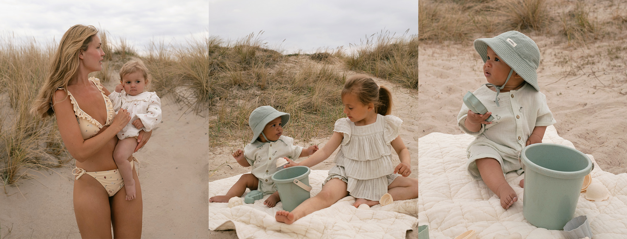 Two children in light green outfits sitting on blanket with bucket on sandy beach.