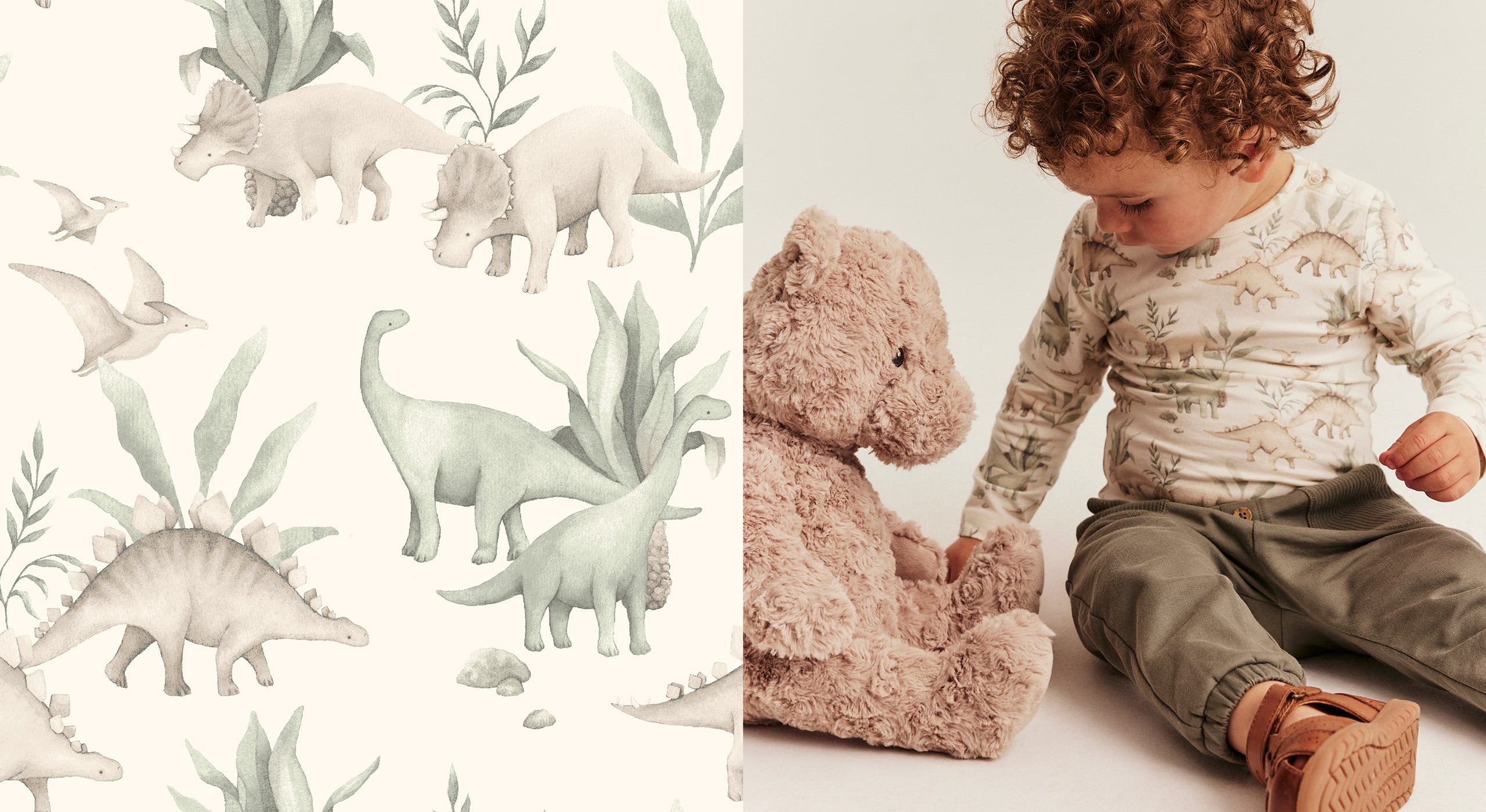 Toddler in beige long sleeve top with dinosaur print and brown pants sitting next to plush teddy bear, dinosaur wallpaper background.
