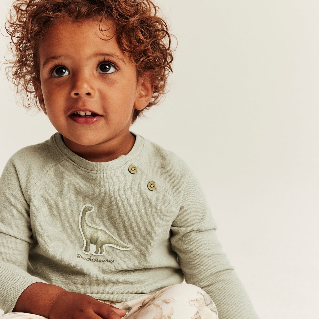 White short-sleeved bodysuit with small fruit print, snap buttons at shoulder, worn by child.