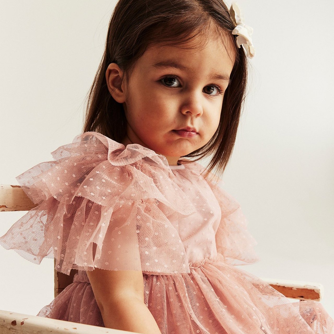 A baby girl wearing a pink chiffon dress with puffy, short sleeves