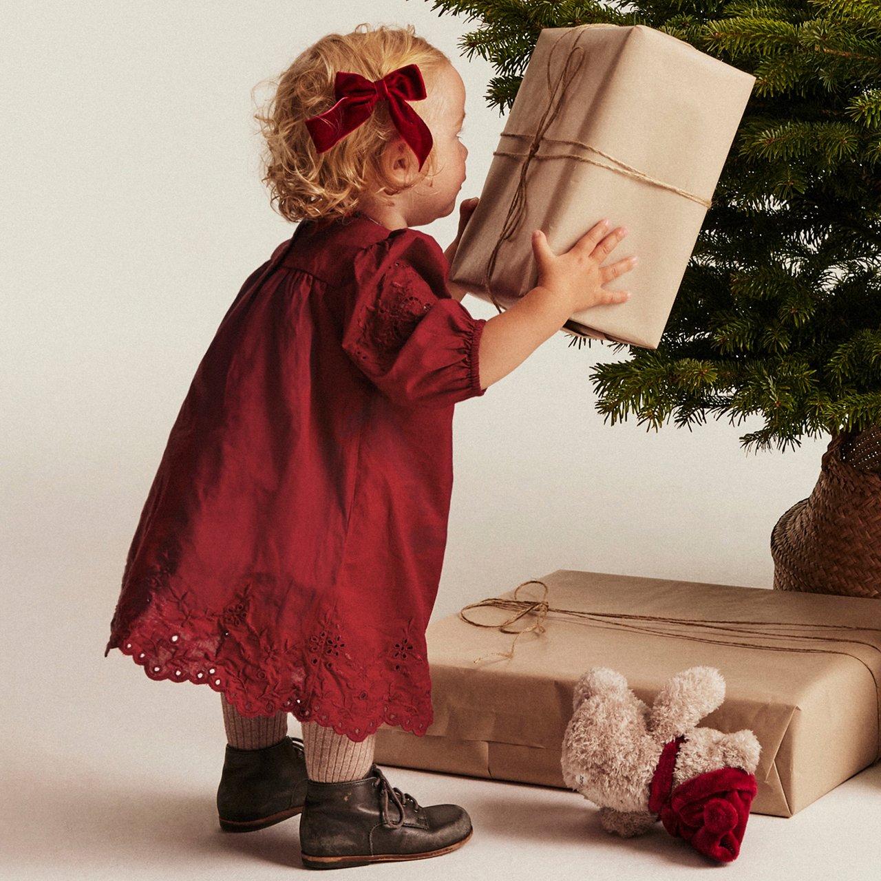 Child in floral dress playing with a teddy bear on a wooden chair.