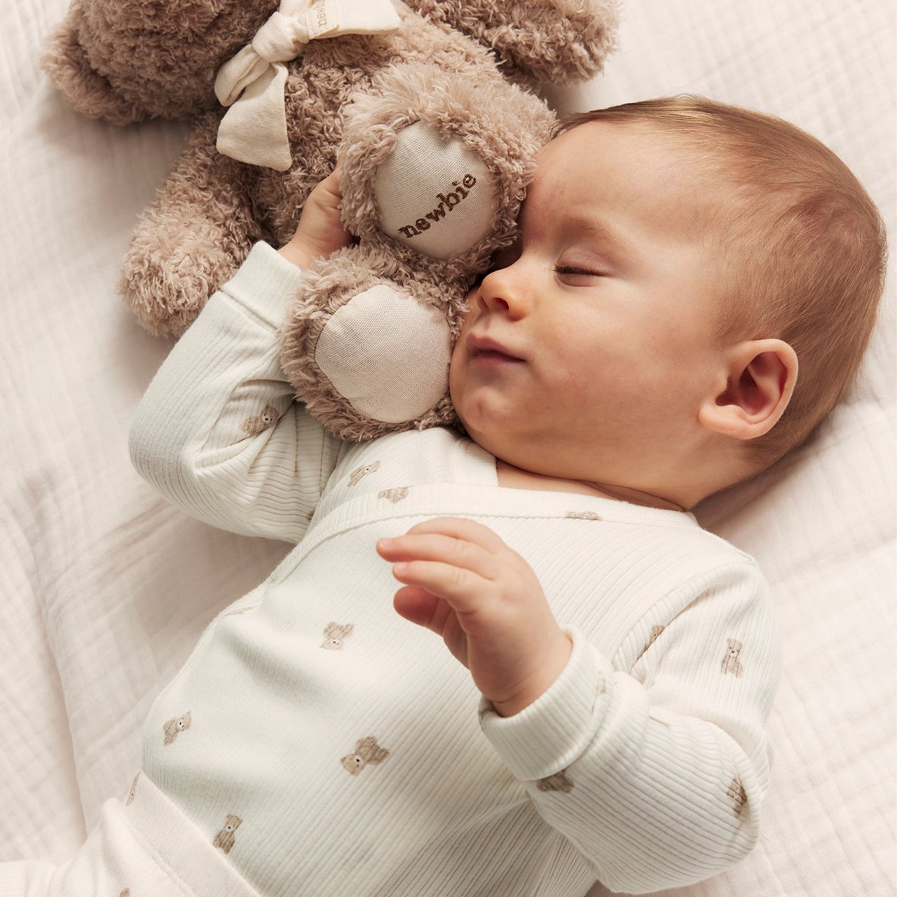 Baby in white bodysuit and a cozy teddy bear