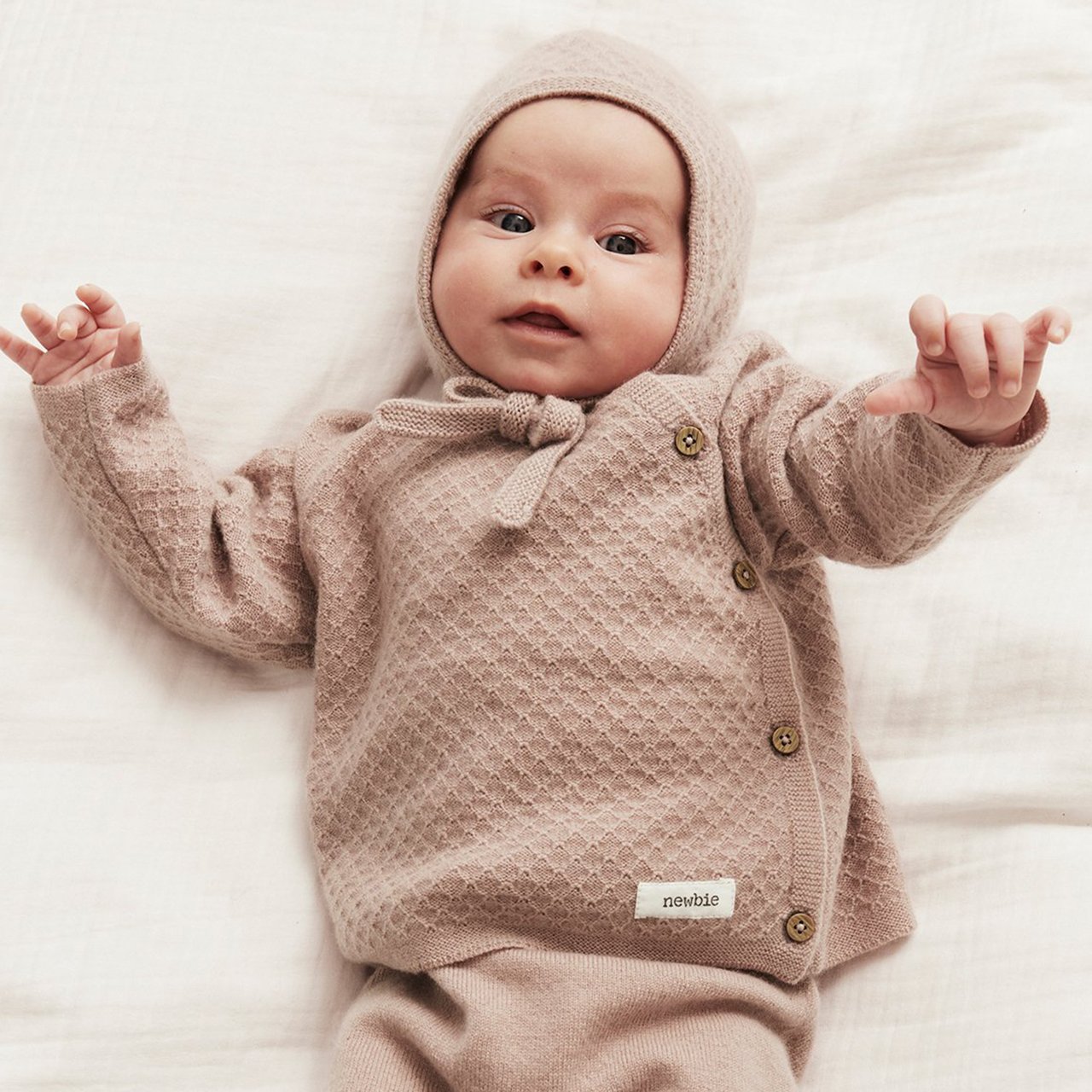 Baby in knitted outfit and bonnet lying on a blanket.