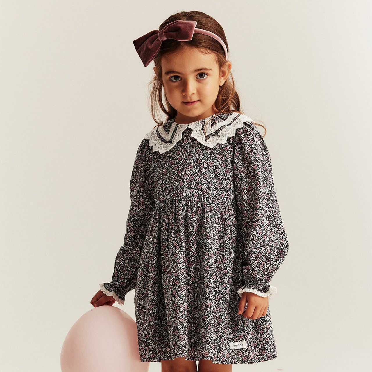 Child in floral dress playing with a teddy bear on a wooden chair.