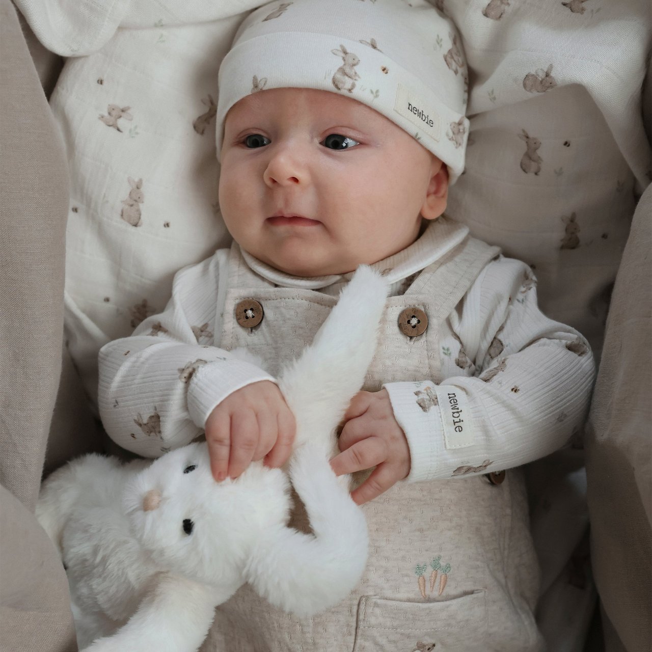 Baby in white bodysuit and hat with rabbit print on it