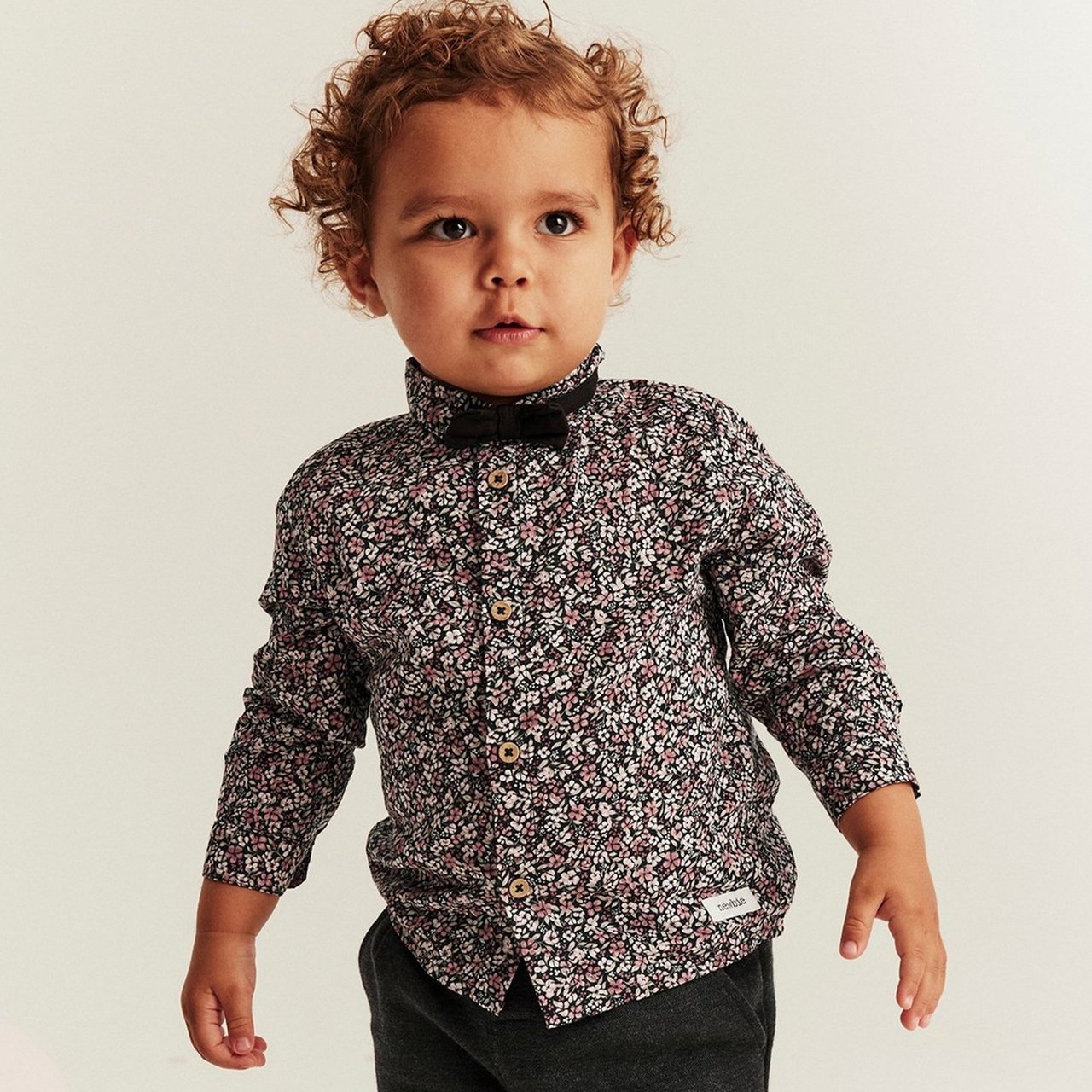 Baby boy wearing a dark shirt with small flower print and a bow tie