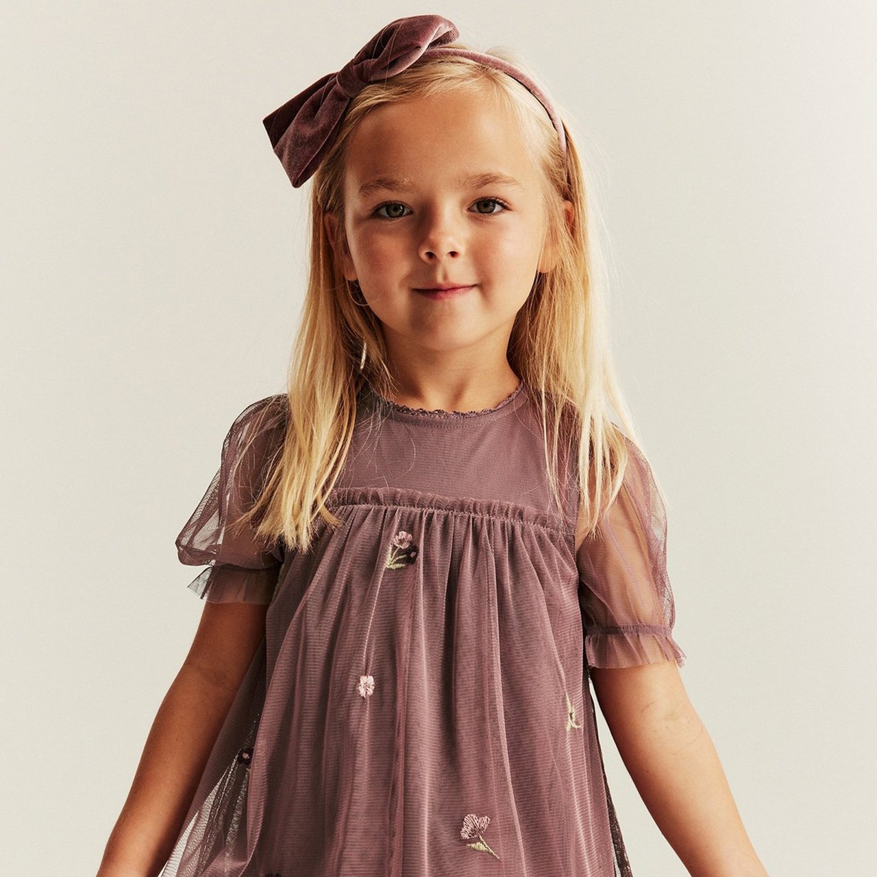 Girl wearing a pink bow hair band and a pink dress with lace and flower details