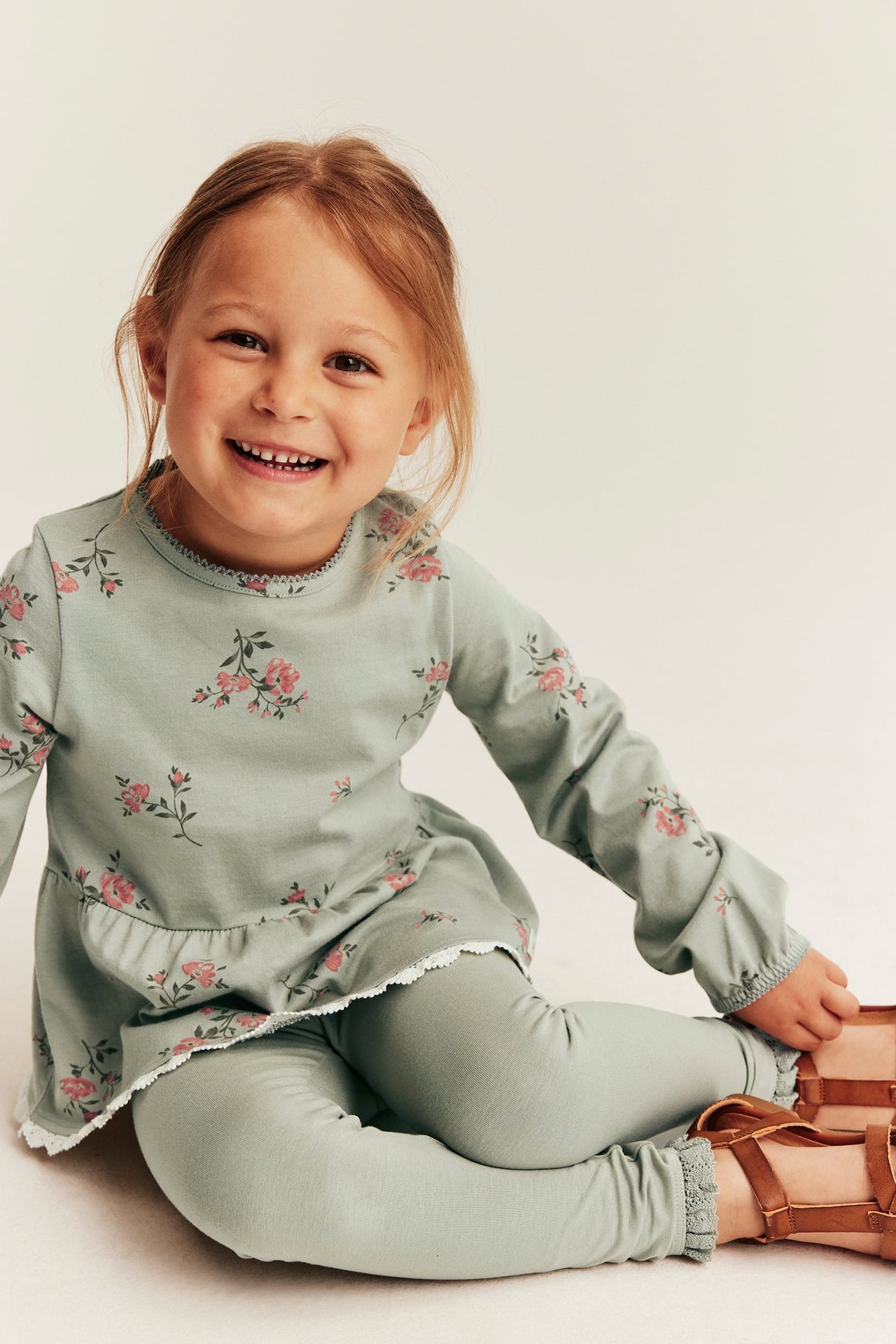 Off-white long-sleeved muslin set with small dinosaur print, front buttons and relaxed fit, worn by child sitting.