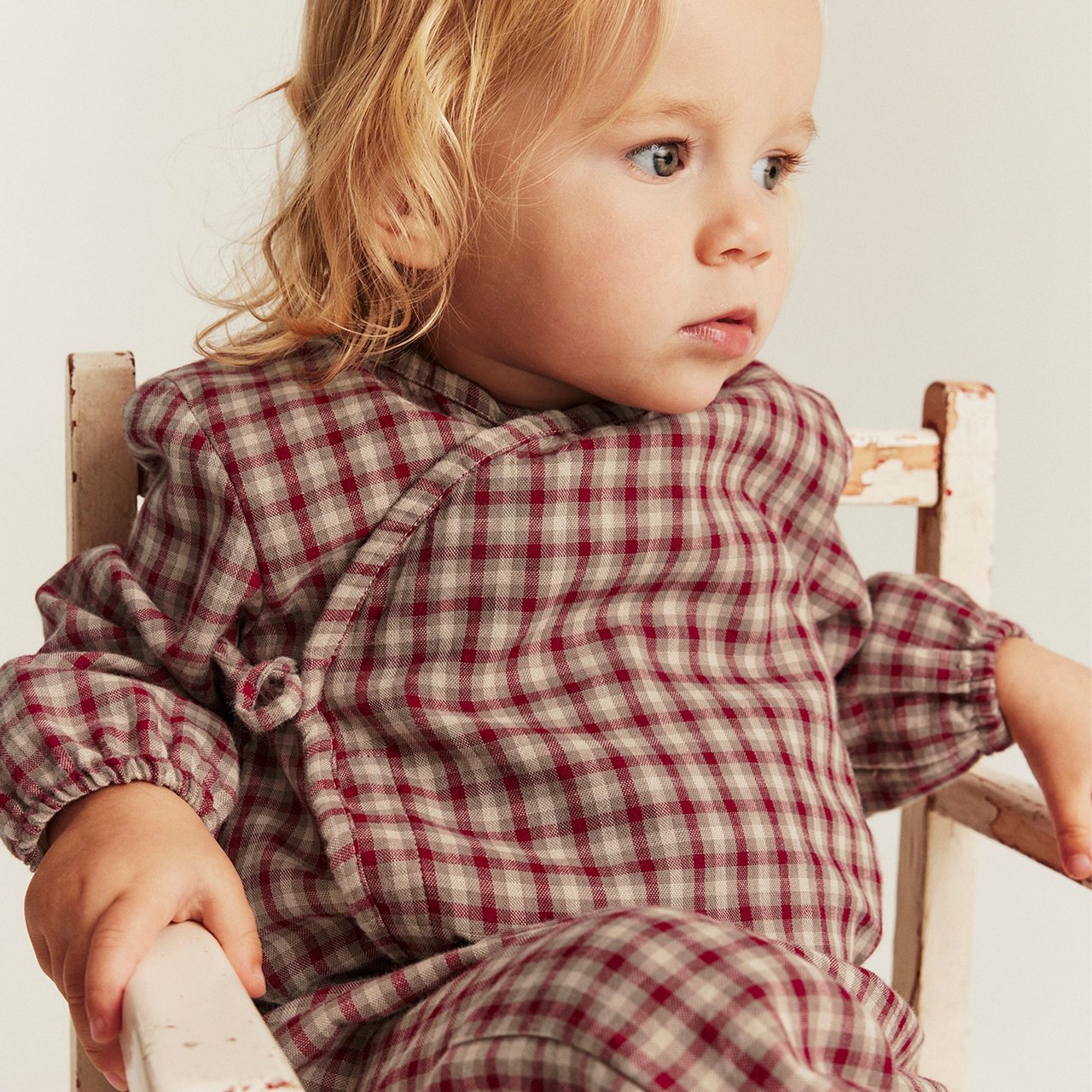 Baby in rot-beiger karierter Pyjama auf einem weißen Holzstuhl.
