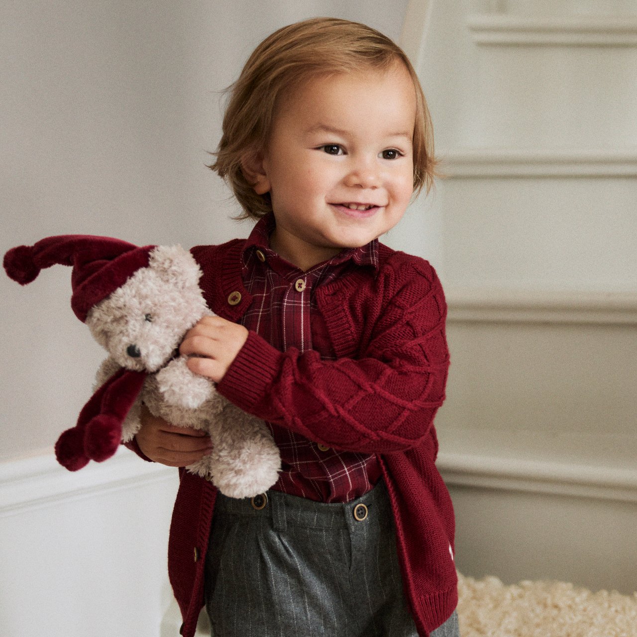 Baby boy wearing a red christmas sweater and holding a teddybear with a santa hat