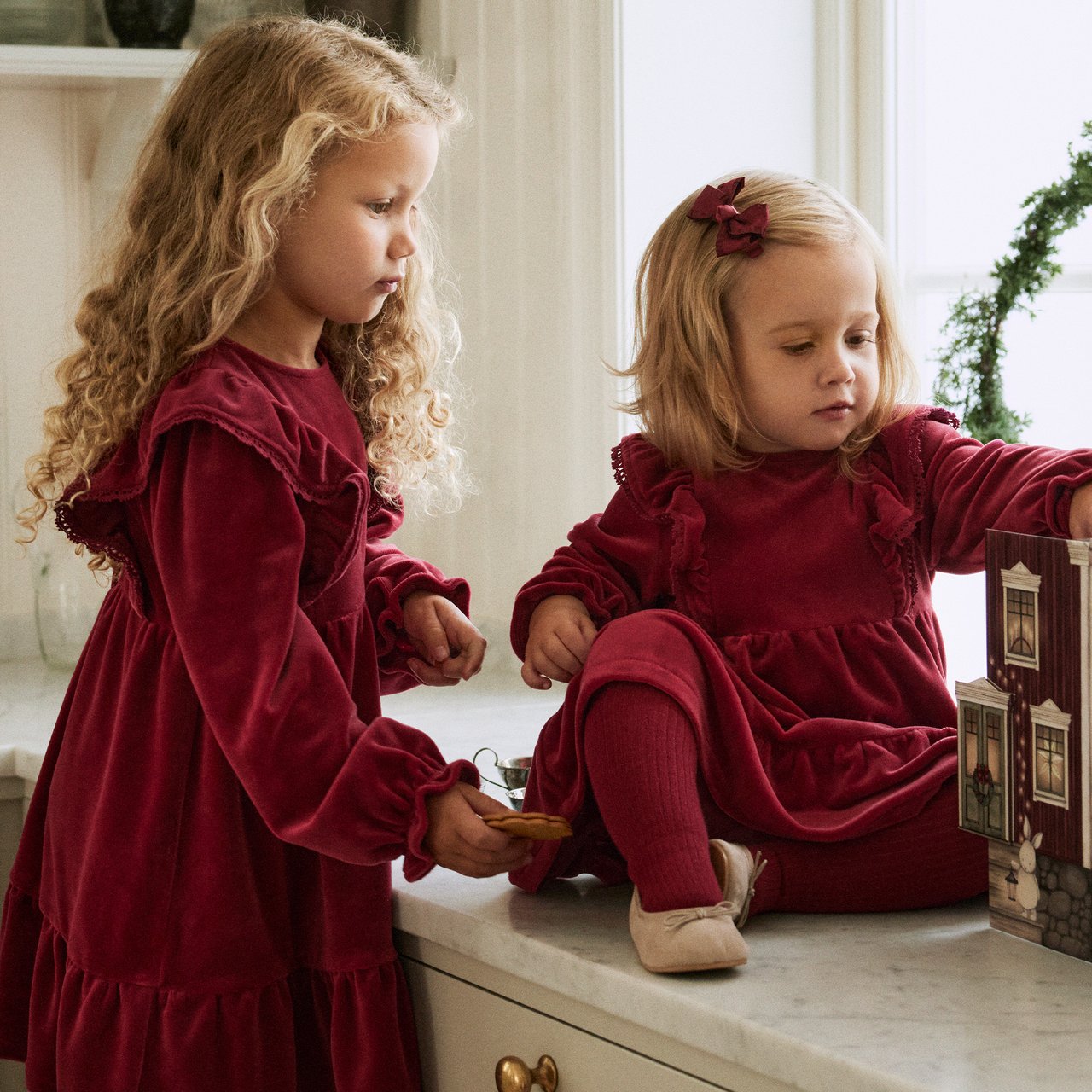 Two children wearing matching red velour dresses