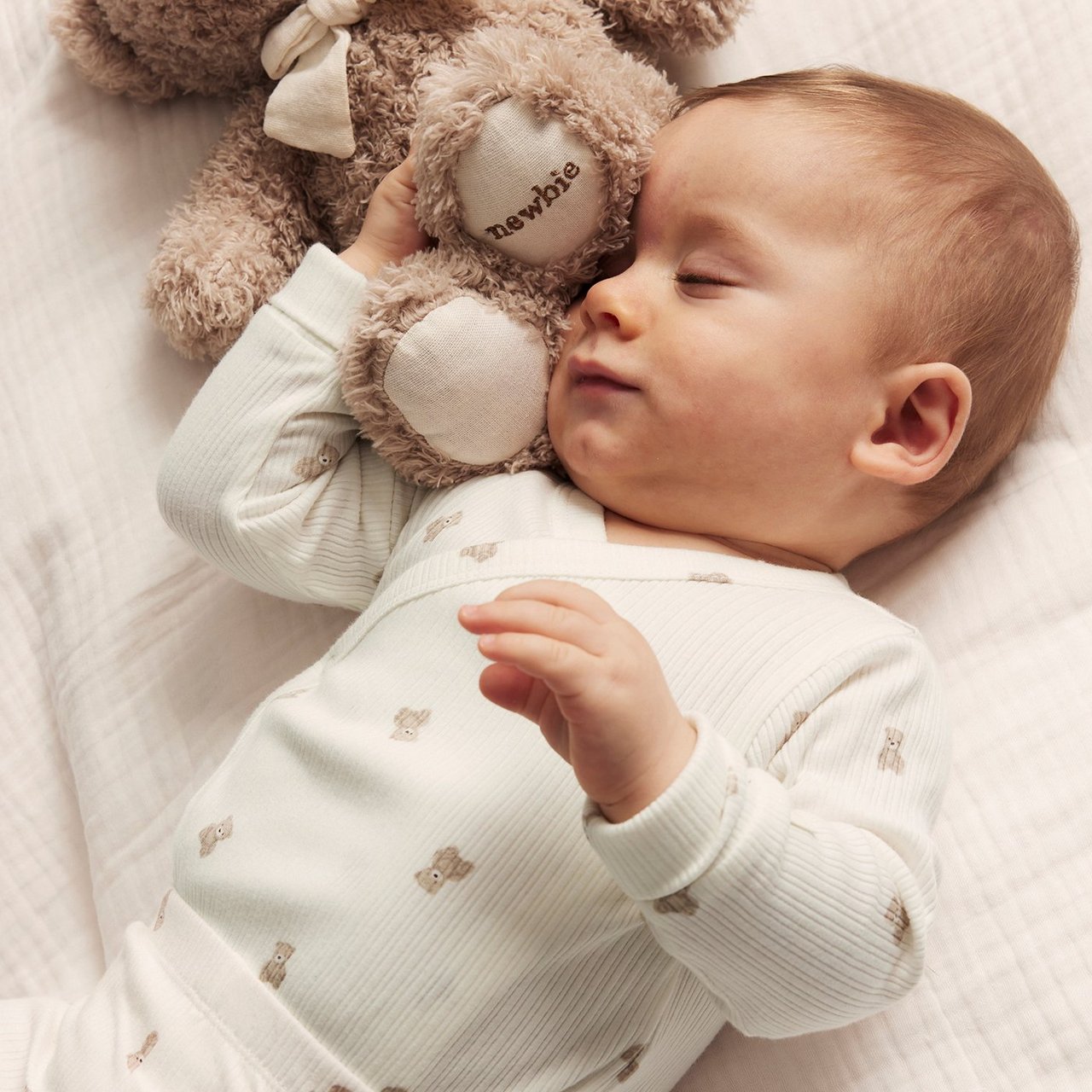 Baby in red knitted christmas sweater holding a teaddybear wearing a santas hat