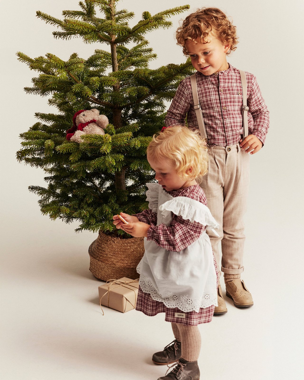 A boy and girl in christmas outfits by a Christmas tree.