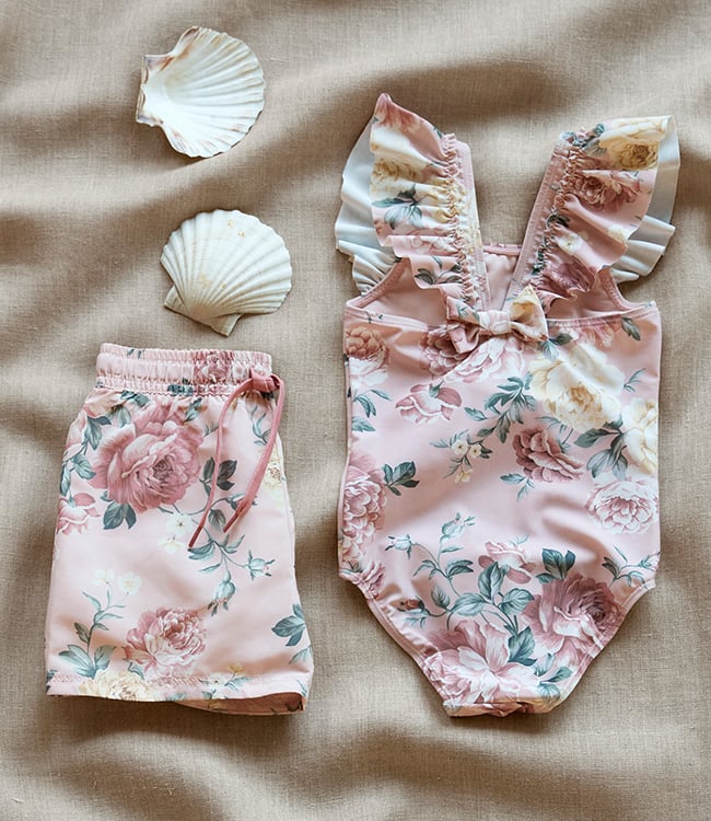 Pink floral toddler swimwear set with swimsuit and swim shorts on beige background.