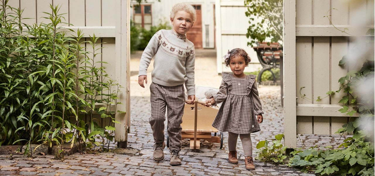 Zwei Kinder ziehen einen Holzwagen durch ein Gartentor.