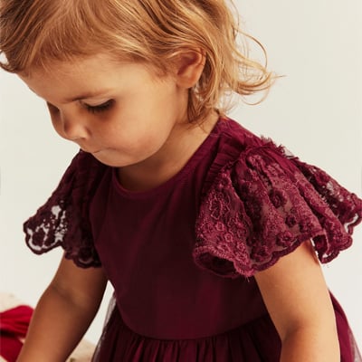 Toddler wearing a burgundy dress with lace ruffle sleeves.