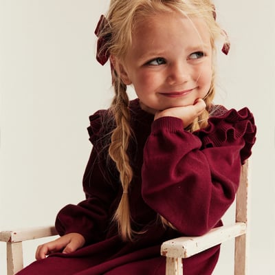 Child in a burgundy dress with ruffle details and braided hair.