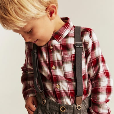 Child wearing a plaid shirt with suspenders in festive seasonal colors.