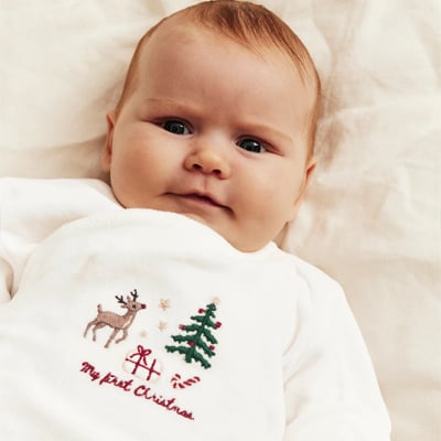 Baby wearing a white outfit with festive holiday embroidery.