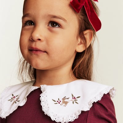 Child wearing a red dress with decorative lace details.
