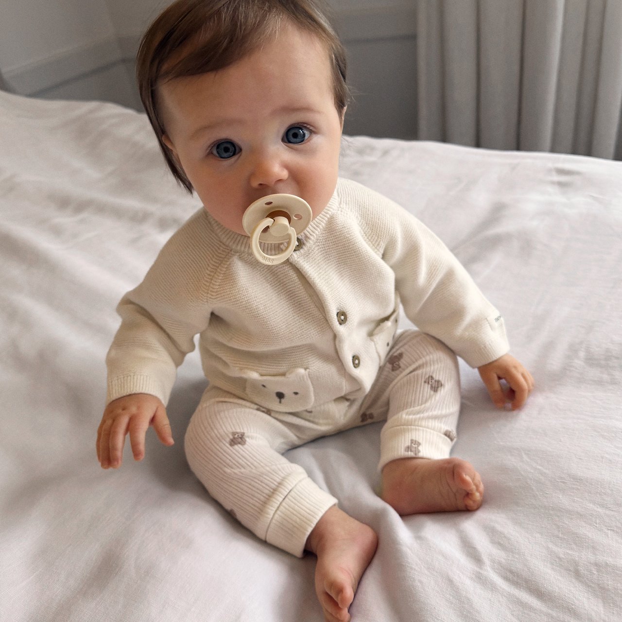 Baby boy sitting on bed in teddy bear clothes