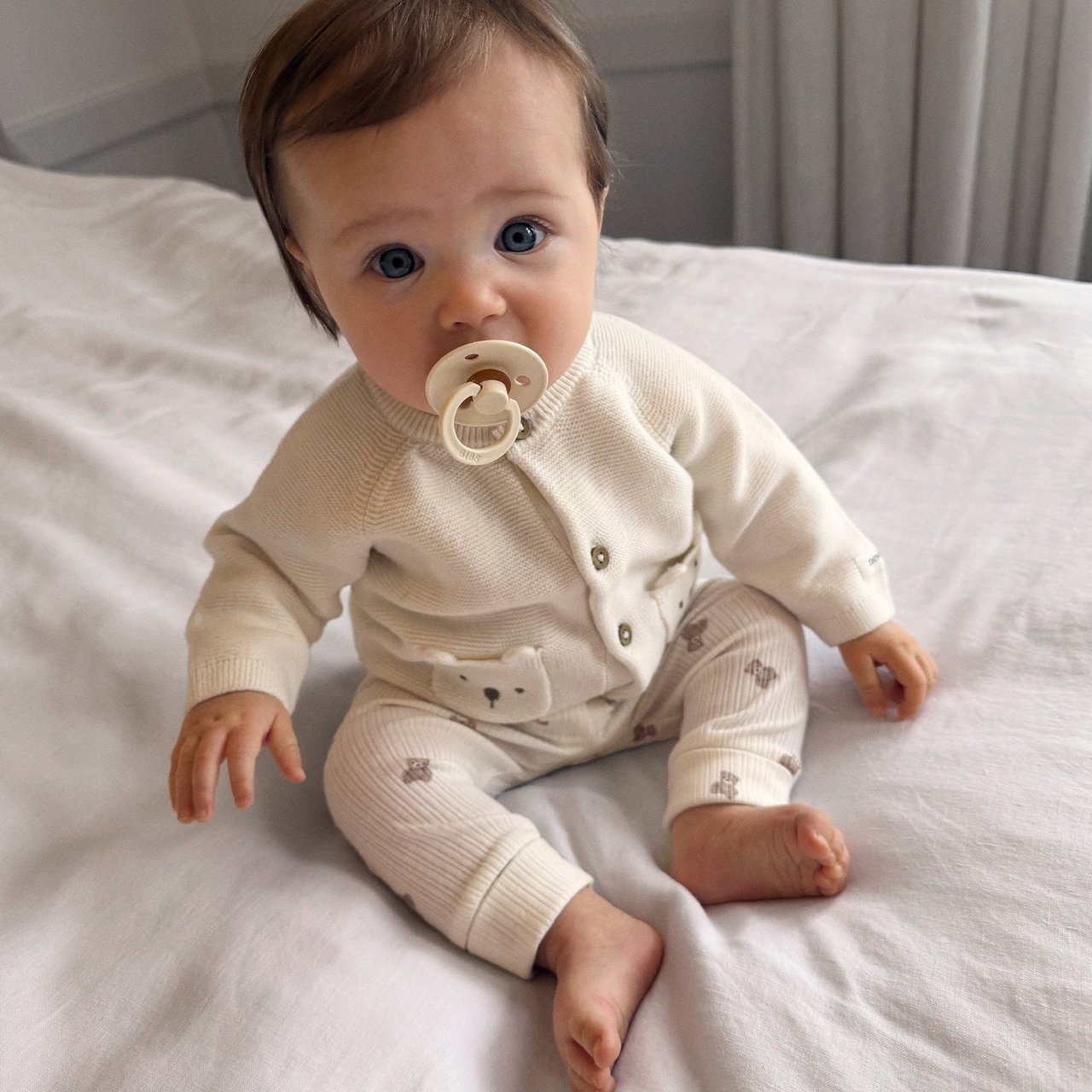 Baby boy sitting on bed in teddy bear clothes