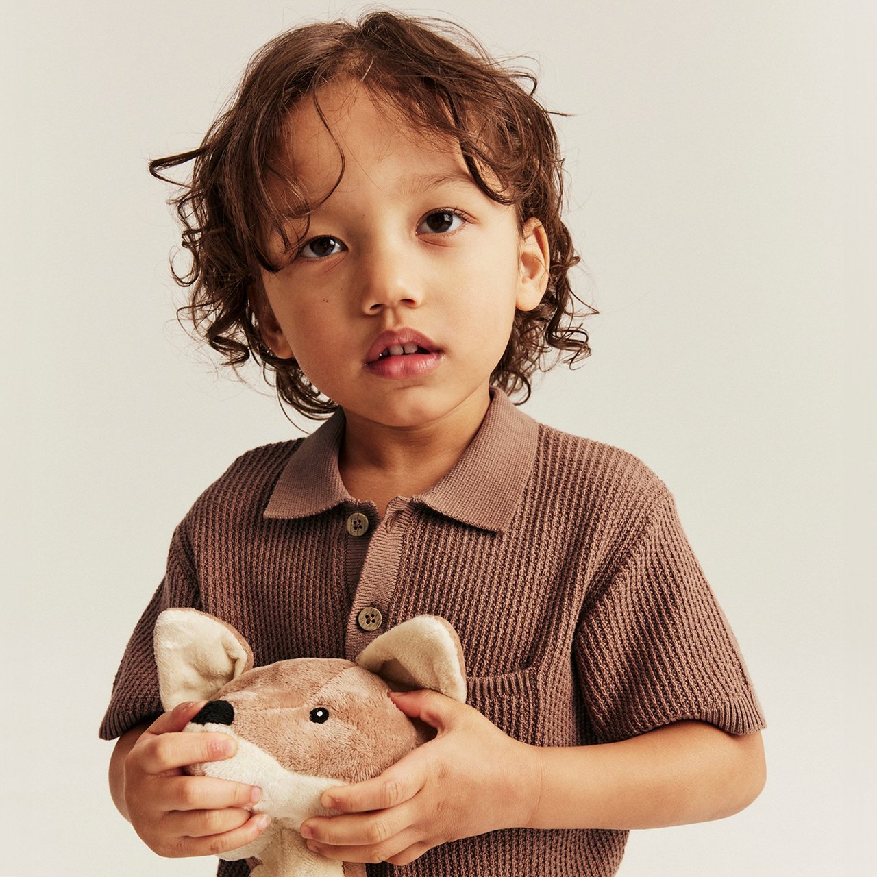Boy wearing a brown knitted polo shirt while holding a soft toy fox