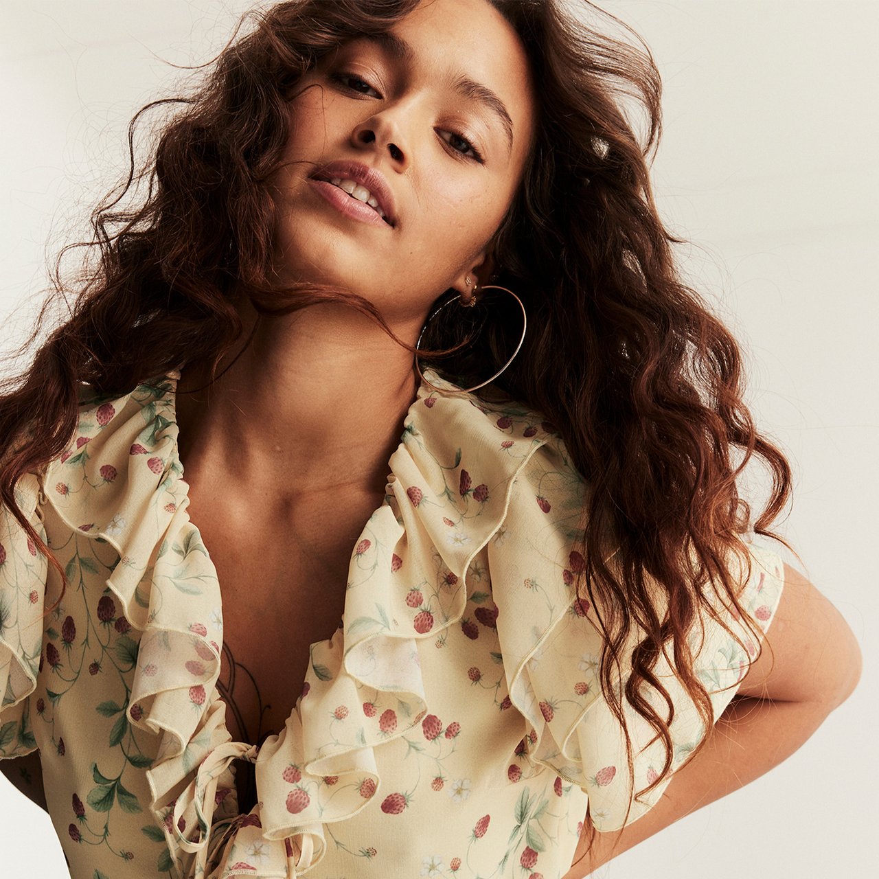 Person wearing a light floral blouse with ruffled details, shown in a close-up against a soft neutral background.