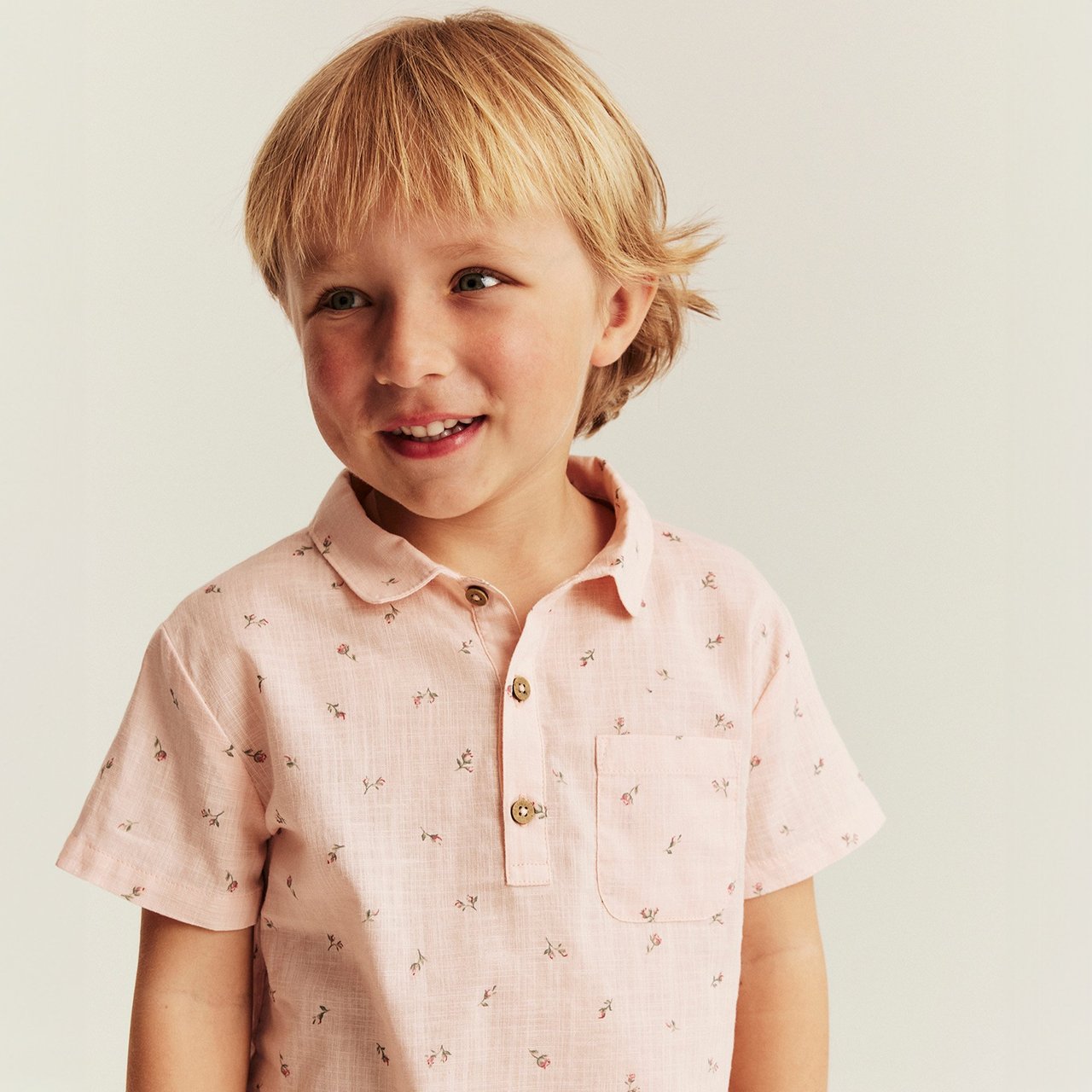 Child wearing a light pink short-sleeve shirt with small printed details and a chest pocket, shown against a light background.