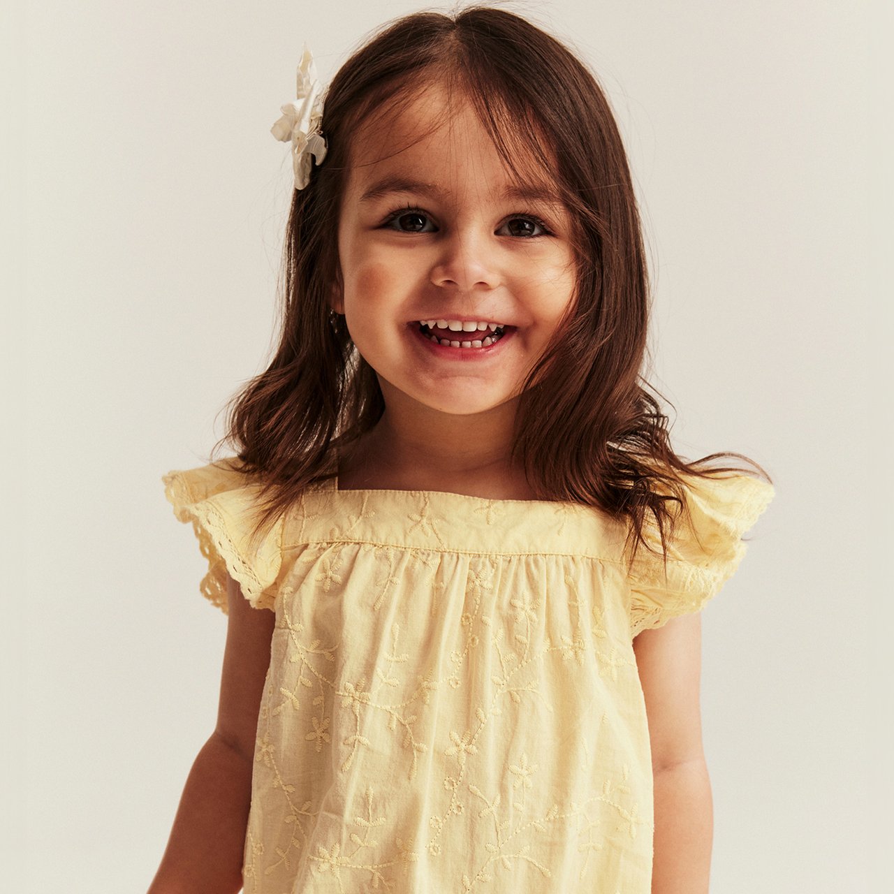 Light yellow short-sleeved jumpsuit with delicate embroidery and ruffle sleeves, worn by child.