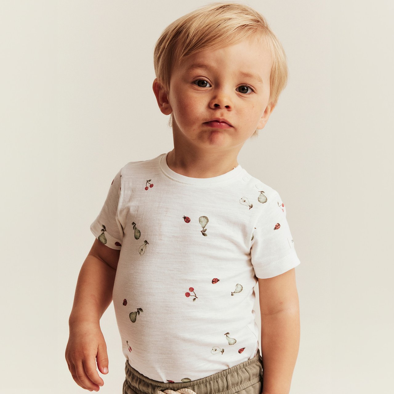 White short-sleeved bodysuit with small fruit print, snap buttons at shoulder, worn by child.