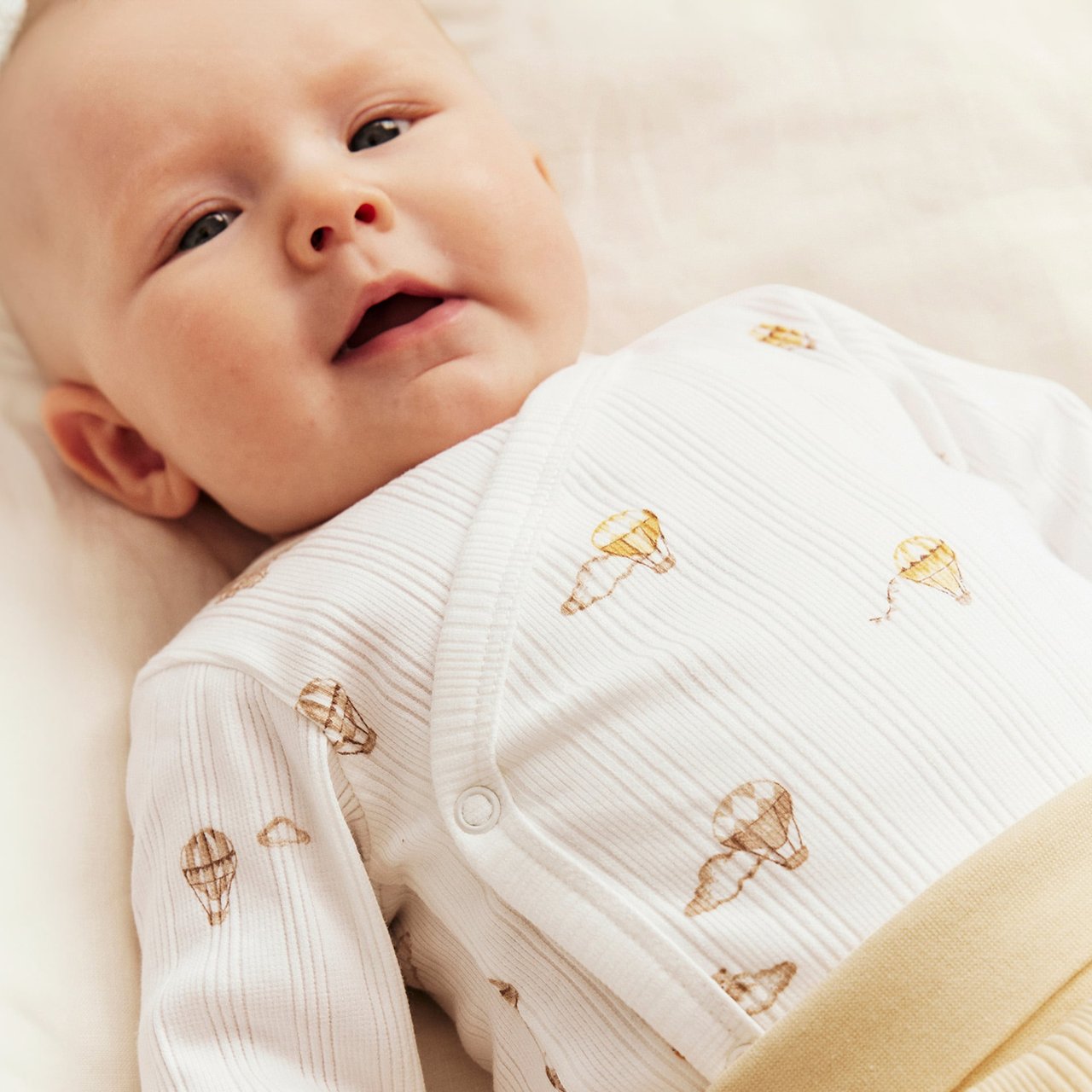 Baby in white wrap-body with hot air balloon print, long sleeves and ribbed cotton fabric.