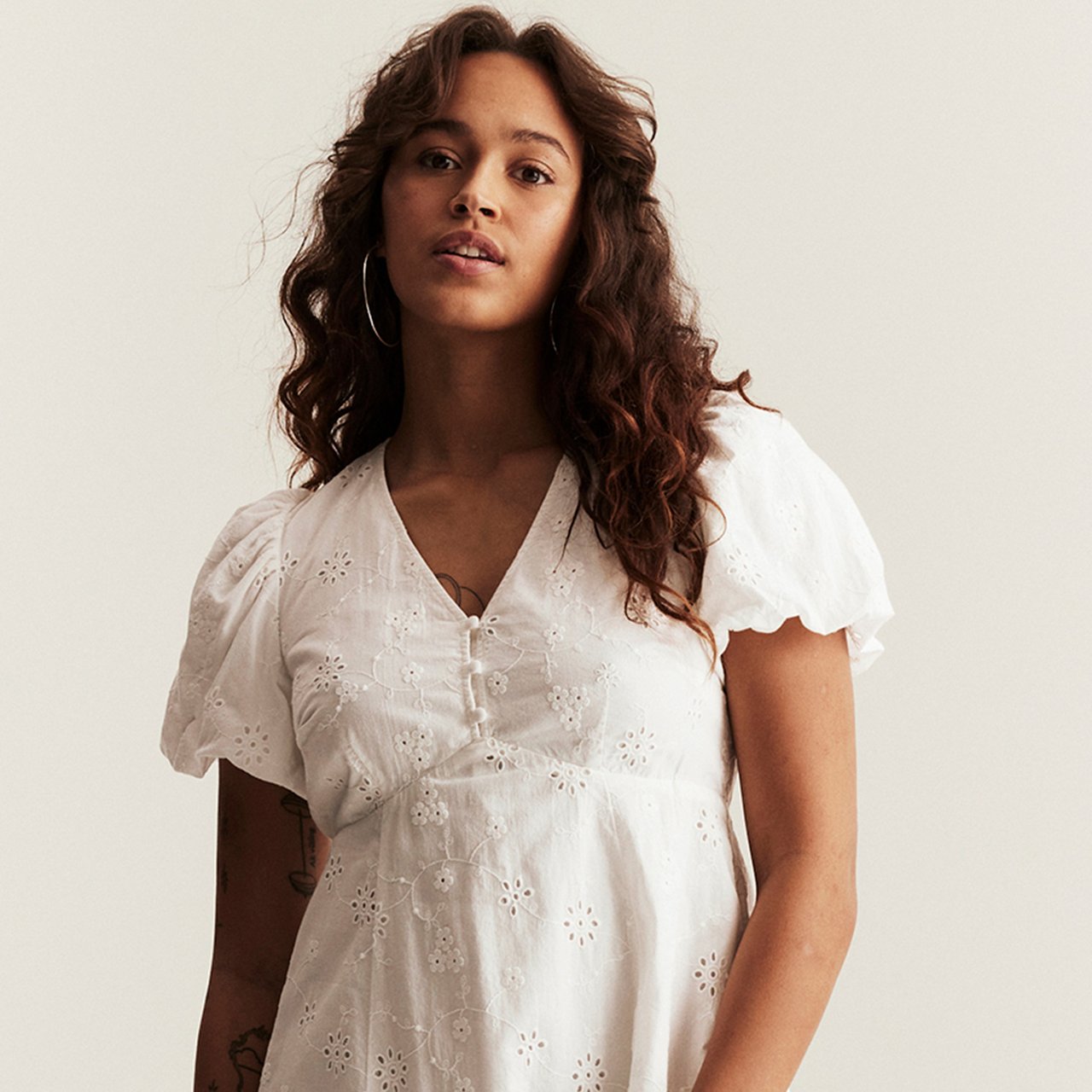 Woman wearing white short-sleeved dress with embroidery anglaise, V-neck and front buttons.
