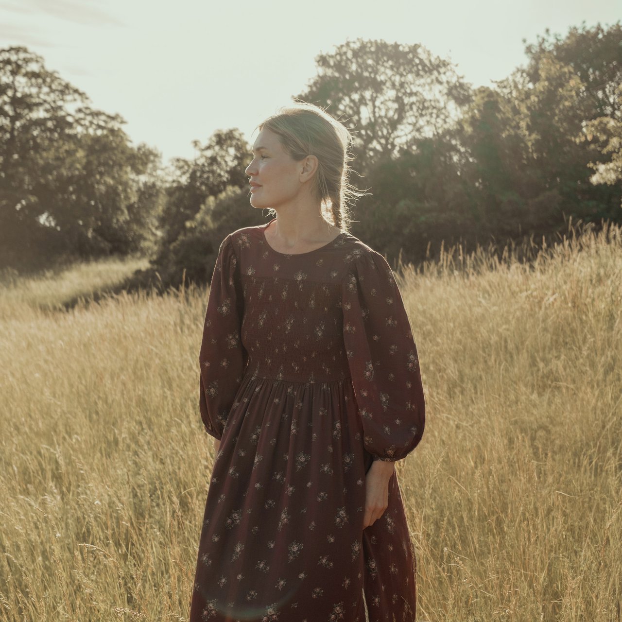 Burgundy floral long-sleeved dress with smocked bodice worn in a grassy field.