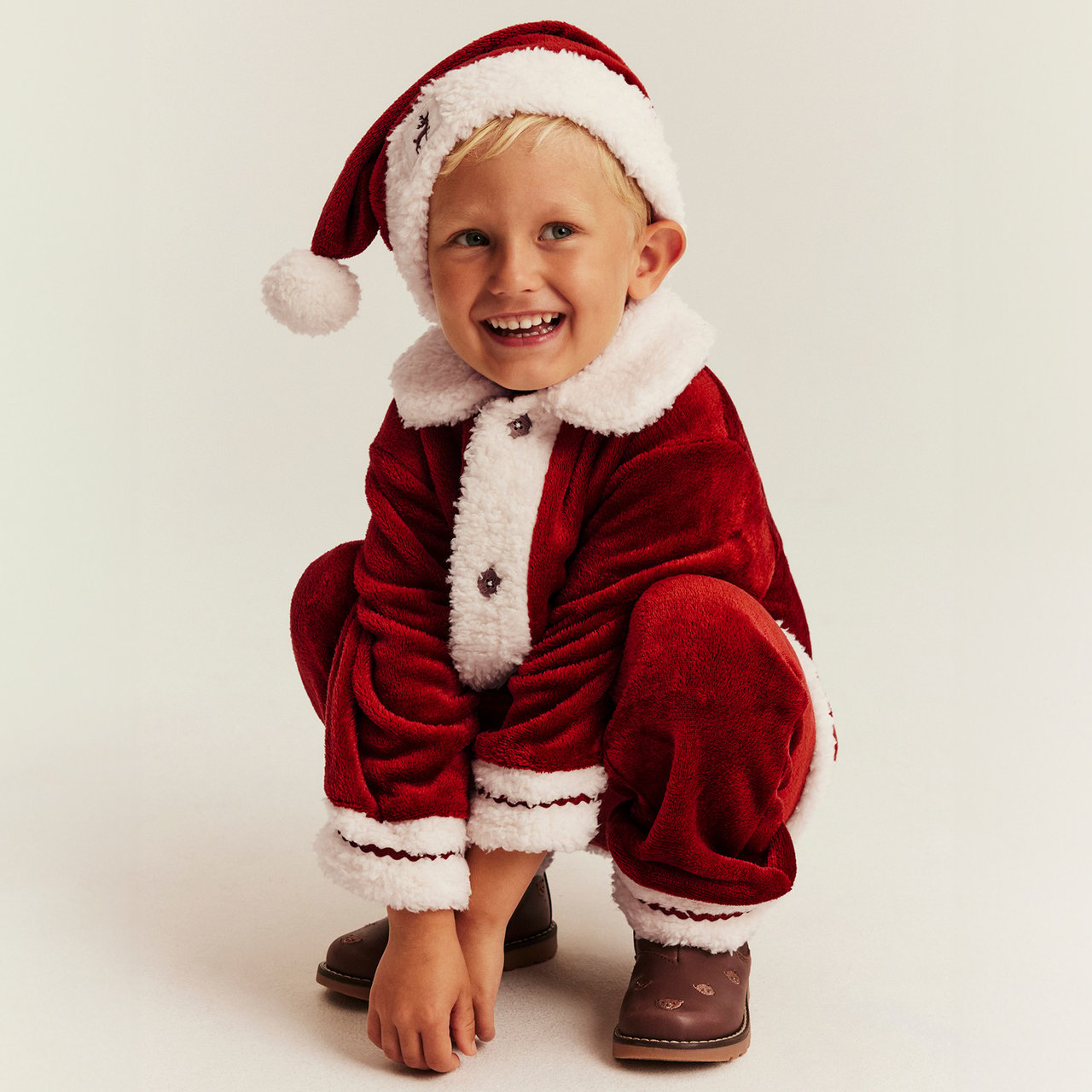Kind in rotem Weihnachtsmannkostüm mit weißem Besatz und passender Mütze auf hellem Hintergrund