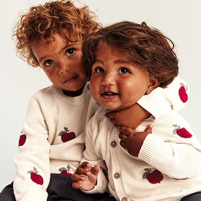 Kinder in cremefarbenem Strickcardigan und Pullover mit Apfelmuster.