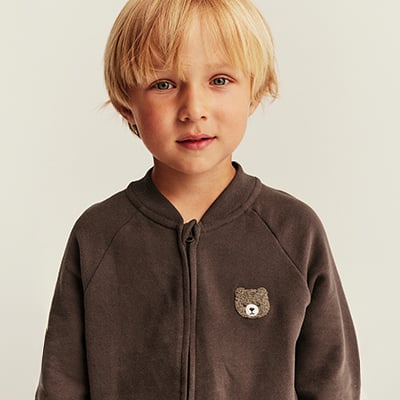 Kind in braunem Sweatshirt mit Teddybär-Motiv.