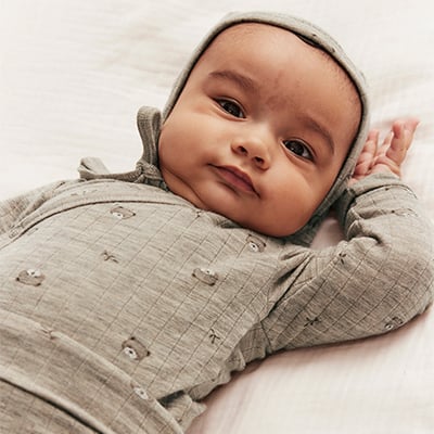 Baby in einem beigen Wollbody und passender Mütze.