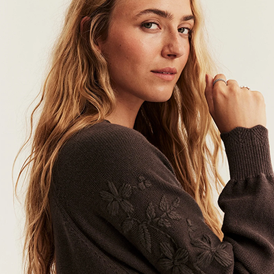 Erwachsene Person in dunkel gestricktem Pullover mit Blumenstickereien an den Ärmeln.