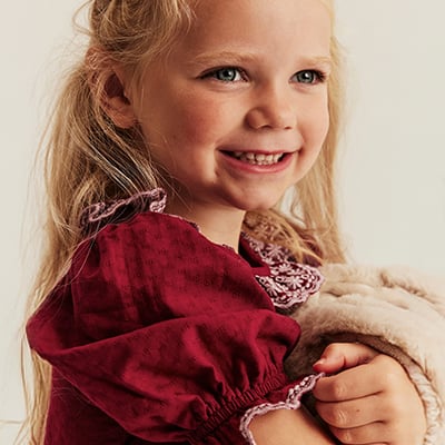 Kind in rotem Kleid mit dekorativen Spitzendetails.