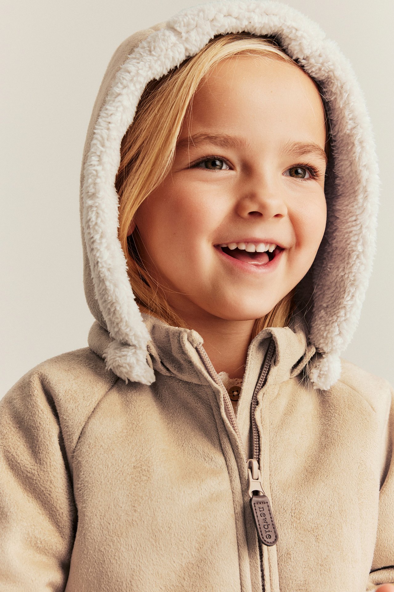 Child wearing a beige sherpa jacket with hood and soft fleece lining, front zip closure