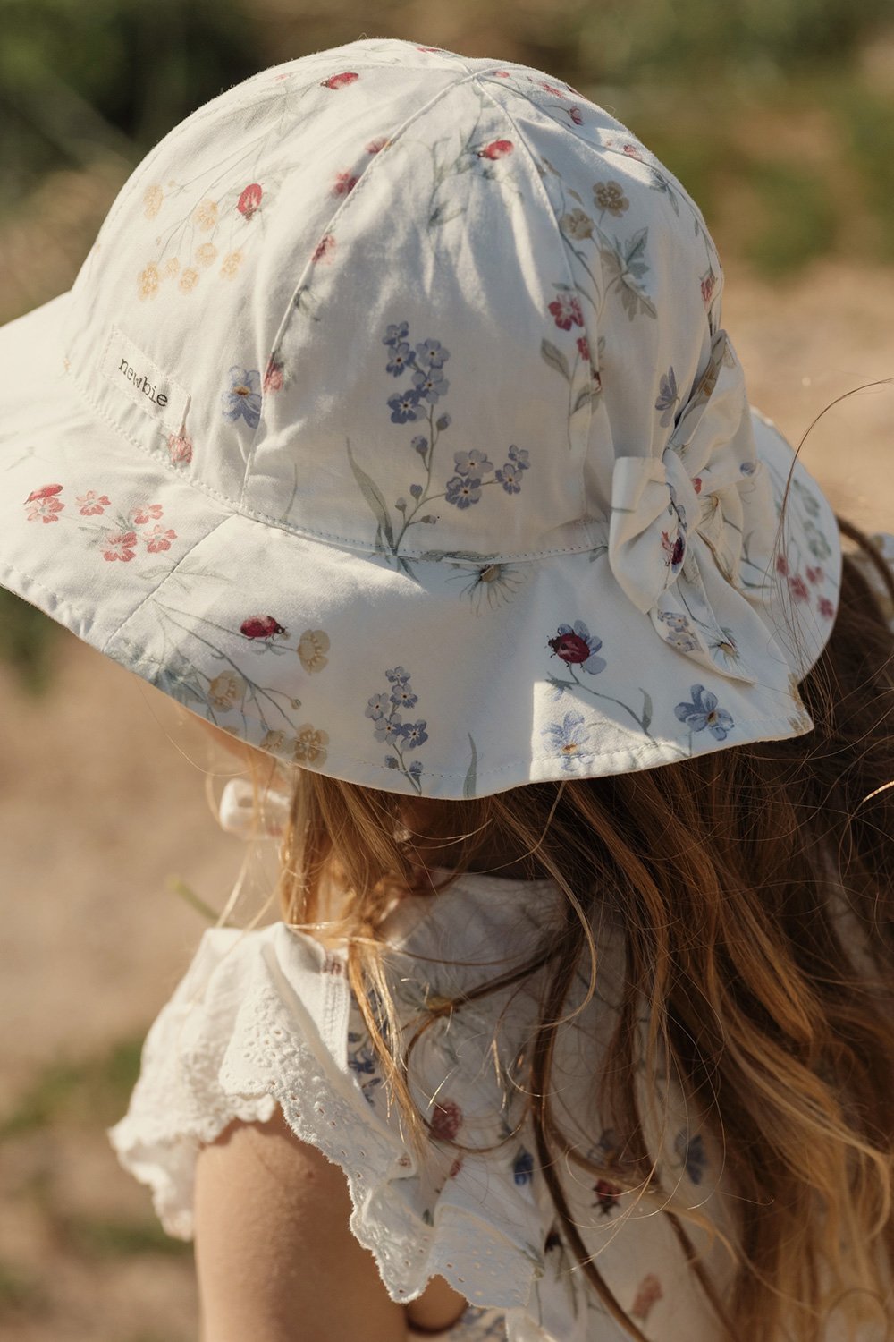 Off-white sun hat with multicolour floral print and tie detail at back, worn on head.