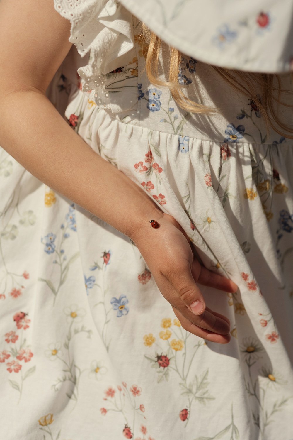 Off-white sleeveless dress with multicolour floral print, close-up of child’s arm with ladybird.