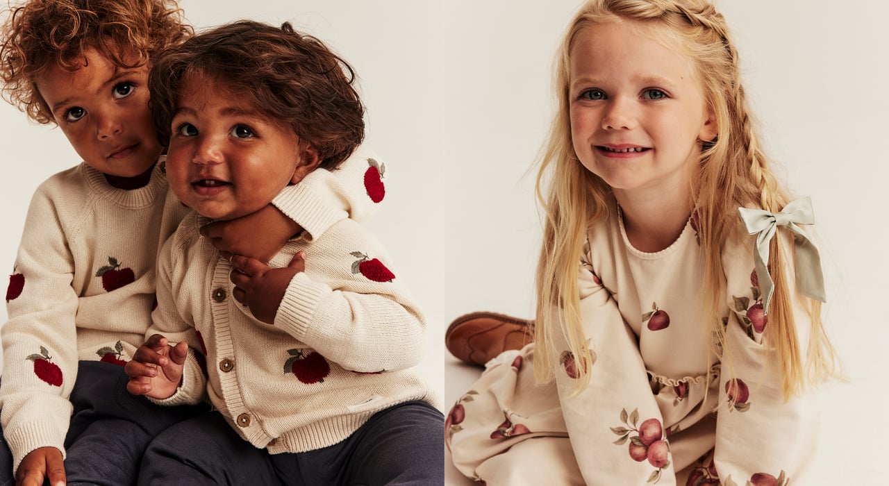 Child wearing a cream sweatshirt with an all-over red apple print against a plain light background.