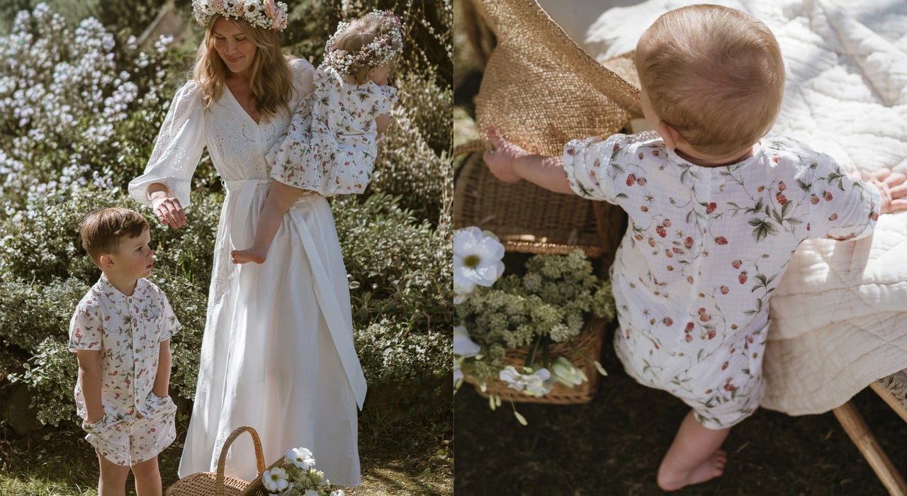 Woman and two children wearing Newbie floral midsummer outfits in a sunlit garden with flowers and picnic details.