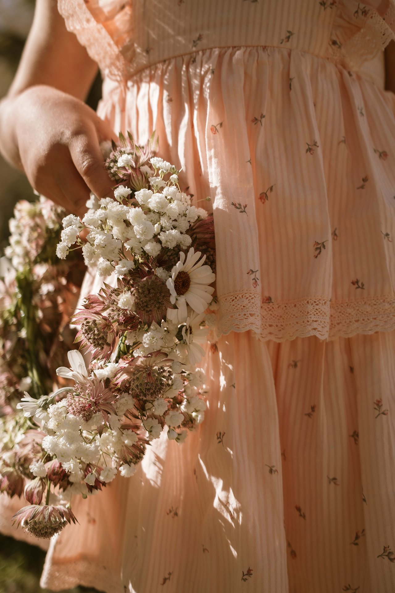 Nahaufnahme eines Kindes mit handgebundenem Blumenkranz und rosafarbenem Sommerkleid.