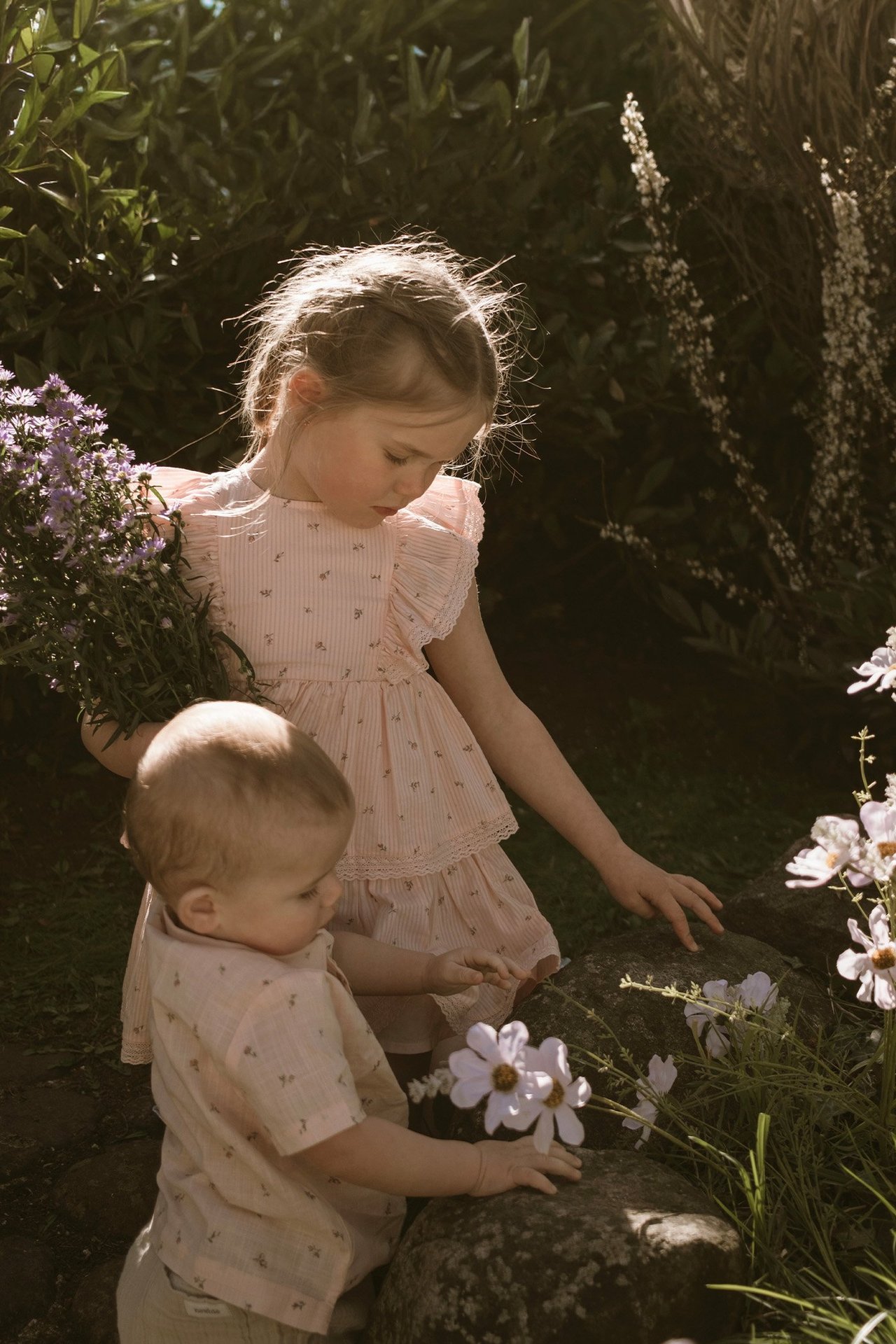 Kinder in leichter Sommerkleidung pflücken Blumen im warmen Abendlicht.