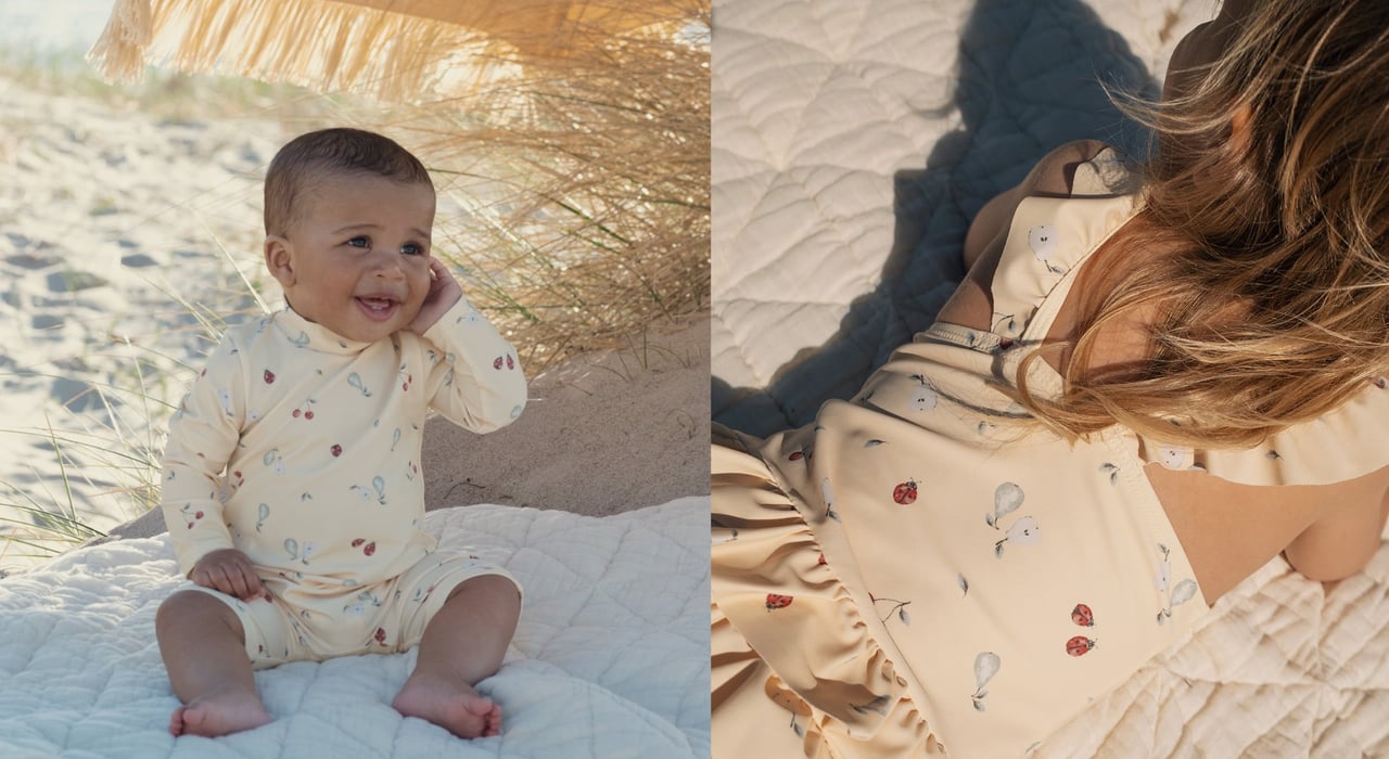 Baby in yellow UV suit with fruit print sitting on blanket outdoors. Child lying on blanket wearing yellow swimsuit with fruit print.